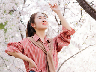 Outdoor portrait of beautiful young Chinese girl in red shirt posing among pink blossom cherry tree brunch in spring garden, beauty, summer, emotion, expression and people concept. 