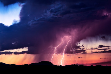 Lightning bolts strike in a storm at sunset.