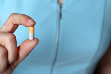 Pill in female hand, doctor with capsule close-up. Woman in blue dress with medication, concept of medical prescription, slimming pills, vitamin or contraceptive