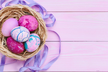 Colorful easter eggs in a nest on pink wooden background