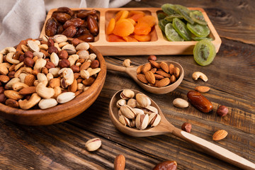 Fototapeta na wymiar Dates, dried apricots and kiwis in a Compartmental dish and assortment of nuts in wooden bowl on a dark wooden table.