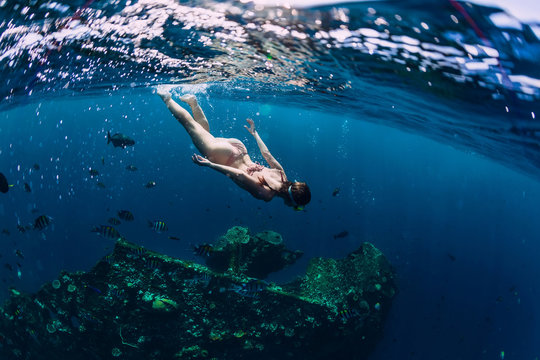 Woman freediver in bikini swin in tropical ocean at shipwreck