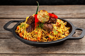 The concept of oriental cuisine. National Uzbek pilaf with meat in a cast-iron skillet, on a wooden table. background image. top view, copy space, flat lay