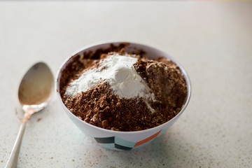 chocolate powder and baking soda in bowl and spoon on kitchen bench