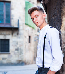 young European guy in shirt and trousers with suspenders walking around city