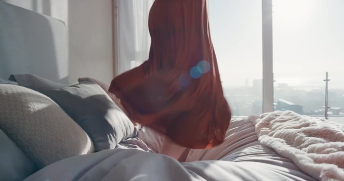 happy woman jumping on bed in hotel room having fun successful lifestyle celebrating enjoying luxury penthouse apartment