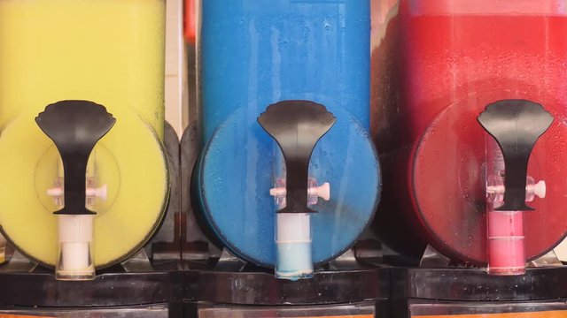 A row of colourful slushes being prepared in slush machines.