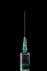 The end of the syringe with a needle filled with liquid on a dark background.