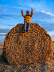 kid throws the straw. boy having fun on the haystack. Haystack in wheat field on blue sky background