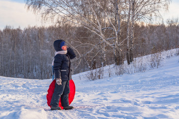 Fototapeta na wymiar child climb the hill with a tube for descent. Children ski in the winter with a slide on the tubing. kid runs to hill and sledding down by the tube. winter leisure