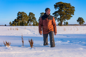 Sports, handsome man walking on a snowy field against a pine forest. Outdoor winter activity and healthy lifestyle