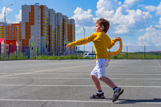 The Boy Throws A Boomerang Into The Blue Sky. The Kid Plays With A Boomerang On The Playground. Children's Outdoor Sports Games