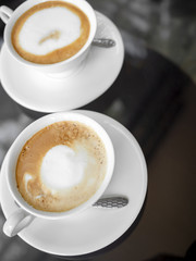 Two white ceramic coffee cups on glass table