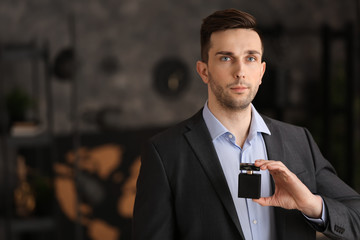 Handsome man with bottle of perfume indoors