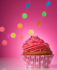 Vanilla cupcake with pink butter cream on bright pink background with garlands