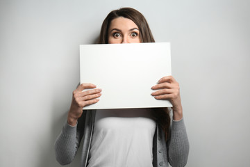 Fototapeta premium Portrait of beautiful woman with blank poster on light background