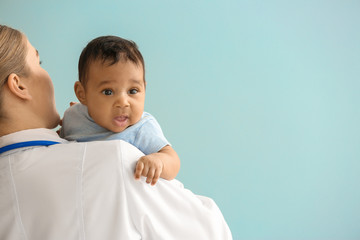 Pediatrician with African-American baby on color background