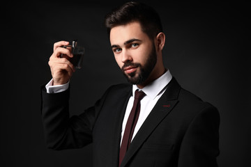 Handsome man with bottle of perfume on dark background