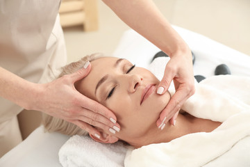 Fototapeta na wymiar Mature woman receiving face massage in beauty salon