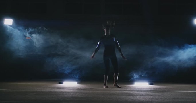 In slow motion in the smoke girl acrobat performs several back flips and coups in the air. Training acrobatic performance. Women's gymnastics competitions.