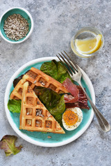Breakfast time. Waffle with prosciutto, salad and egg for breakfast on a concrete background. View from above.