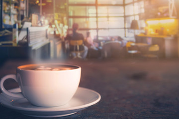 Cappuccino cup on the table with blur people in coffee shop background, vintage tone