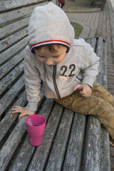 A little boy is drinking tea on the bench.