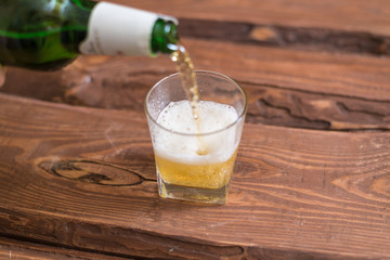 Beer is poured into a glass from a bottle on a wooden background.