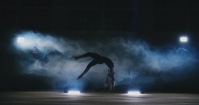 In slow motion in the smoke girl acrobat performs several back flips and coups in the air.