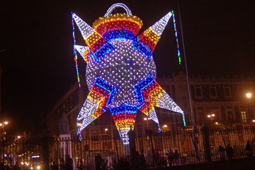 Brightly lit New Year's Eve decoration with white, orange, red and blue lights and dim streetlights in background at night on streets in Mexico City