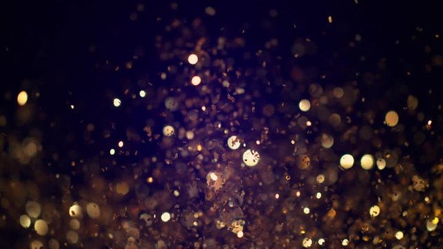 Golden glitter explosion in super slow motion on blue background.