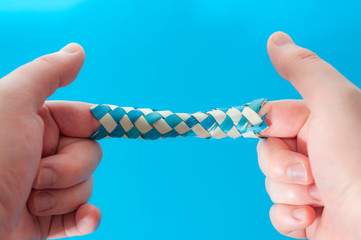 Puzzle game and logic games concept with hands playing with a chinese finger trap, a toy that the more you pull the tighter it gets stuck and you need to push to escape isolated on blue background