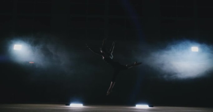 In slow motion in the smoke girl acrobat performs several back flips and coups in the air. Training acrobatic performance. Women's gymnastics competitions.