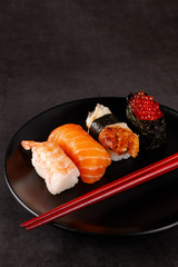 Concept of Asian cuisine. Japanese sushi with soy sauce on a black plate, on a black background. Red Chinese sticks. copy space