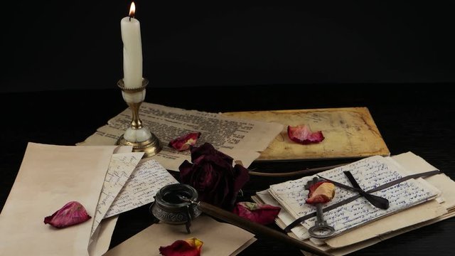 Burning candle in a candlestick on the background of the dried rose, a key, an old letters, envelopes and inkwell with a pen. Memory, family archive