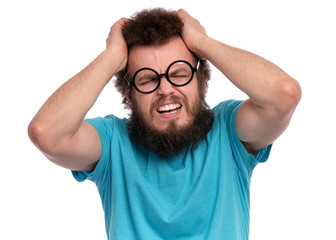 Crazy bearded Man with funny Curly Hair, in eye Glasses, suffering from headache. Upset unhappy Sick guy squeezing head with hands, writhing in pain. People, healthcare, stress or migraine concept