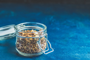 Open glass jar of organic granola on a dark blue concrete table