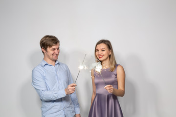 Party, family and holidays concept - young couple celebrating their anniversary with sparklers on white background