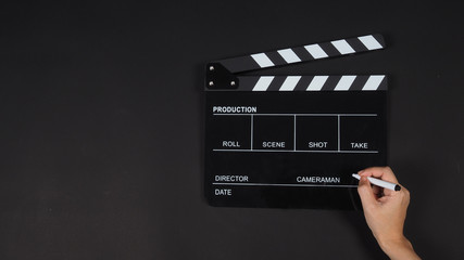 Fototapeta na wymiar Black Clapperboard or clap board or movie slate use with right hand holding pen in video production ,film, cinema industry on black background.