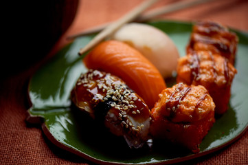 Japanese traditional cuisine on handmade ceramics. Plate in the form of green leaf, orange background. Rolls and sushi .