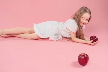 Obraz na płótnie Canvas cute funny little girl in white dress with red big apple on pink background