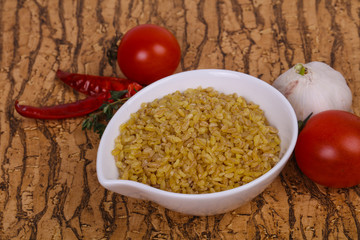 Raw bulgur in the bowl with tomatoes and garlic