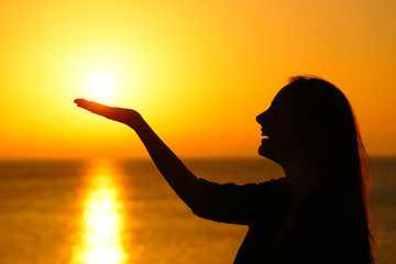 Woman profile holding sun at sunrise on the beach