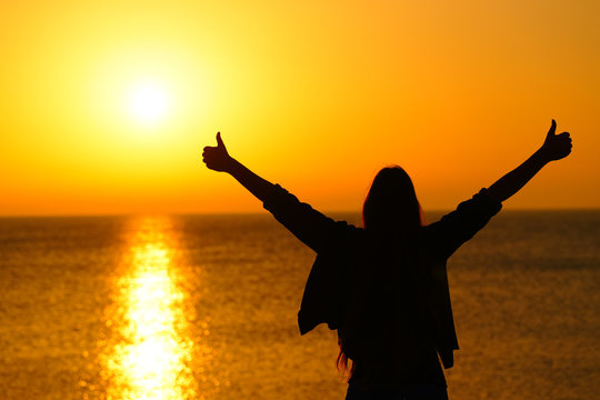 Happy woman with thumbs up celebrating sunrise