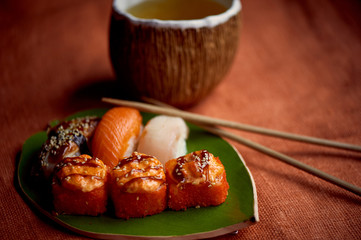 Japanese traditional cuisine on handmade ceramics. Plate in the form of green leaf, orange background. Rolls and sushi .