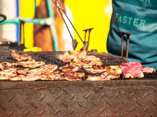 Unrecognizable person cooking pork meat on a barbecue in the street at a popular party in a village in Spain