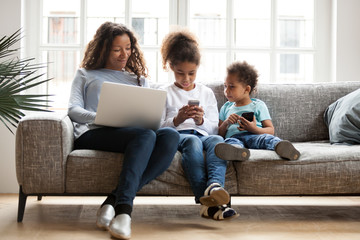 Young black family sit on couch using gadgets