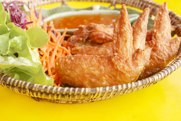 Close up of crispy fried chicken wings with sauce and vegetable salad  in bamboo basket on colorful yellow table.