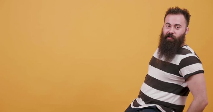 Young bearded man having fun on a rotating chair in front of yellow background. Monocolor background and a young man playing and being joyful.