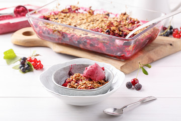 Apple and berry crumble with oats served with fruit ice-creame on white table. Crispy fruit pie, healthy summer dessert. Close-up.